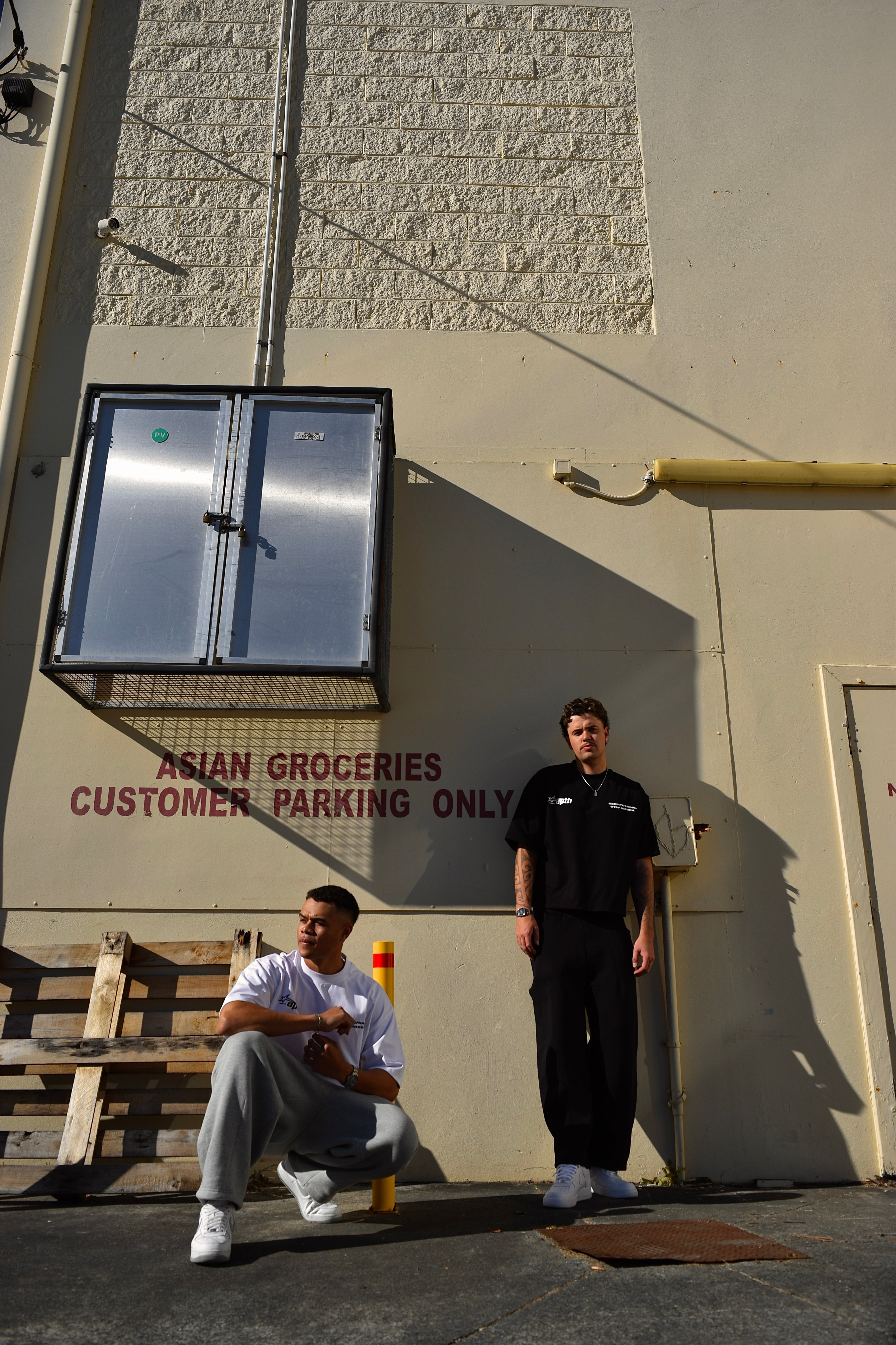 Two men standing outside a building with a sign indicating 'Asian Groceries Customer Parking Only'.